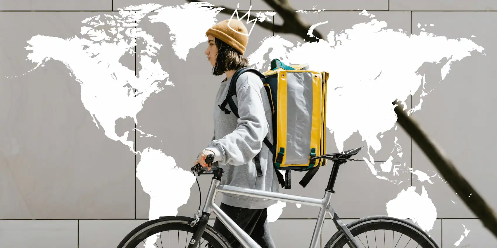 A girl with a backpack walking with her bicycle next to door with world map.